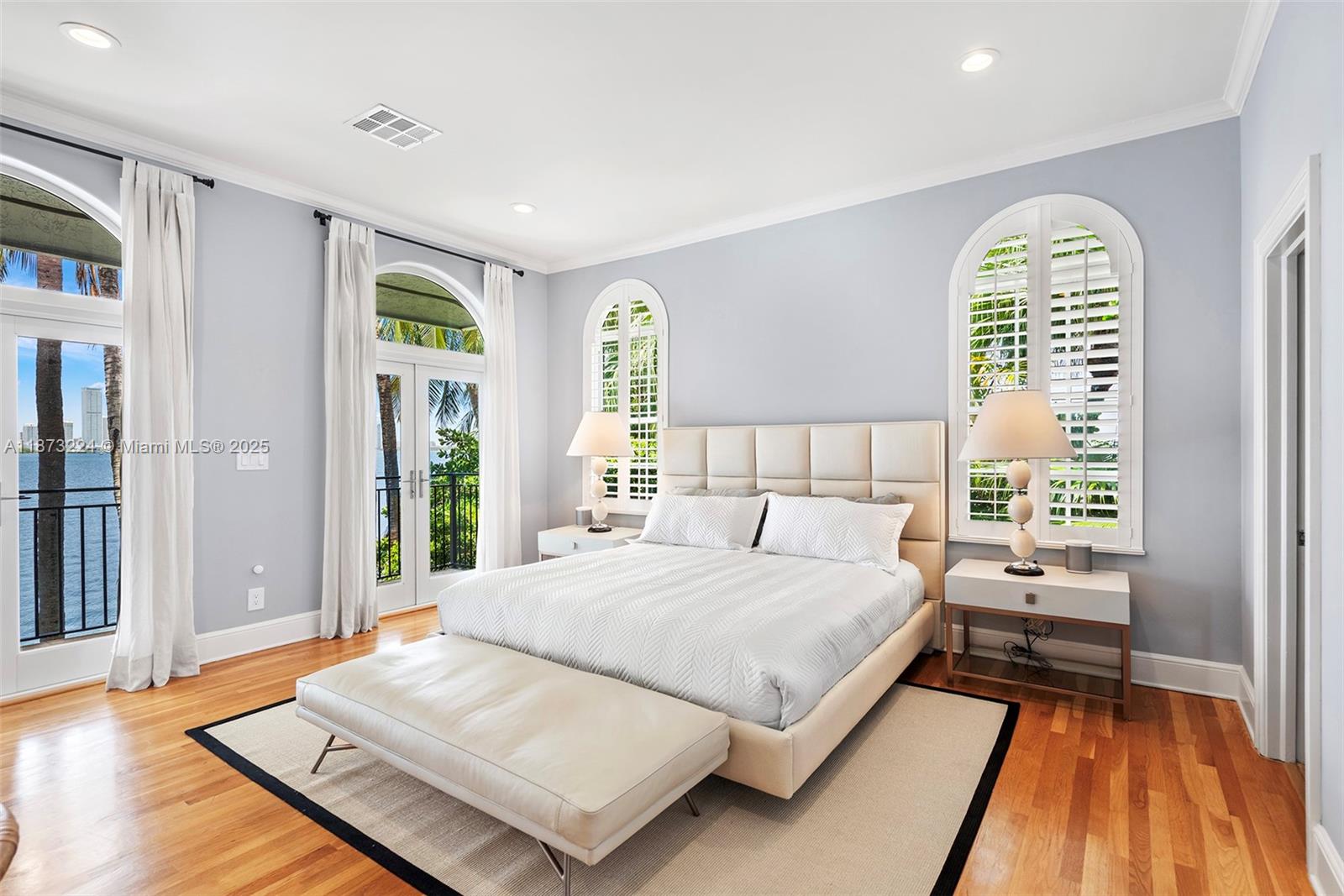 A bedroom features a bed, two nightstands, arched windows with shutters, and hardwood flooring — 814 W Dilido Dr, Miami Beach FL 33139, MIAMI BEACH, FL