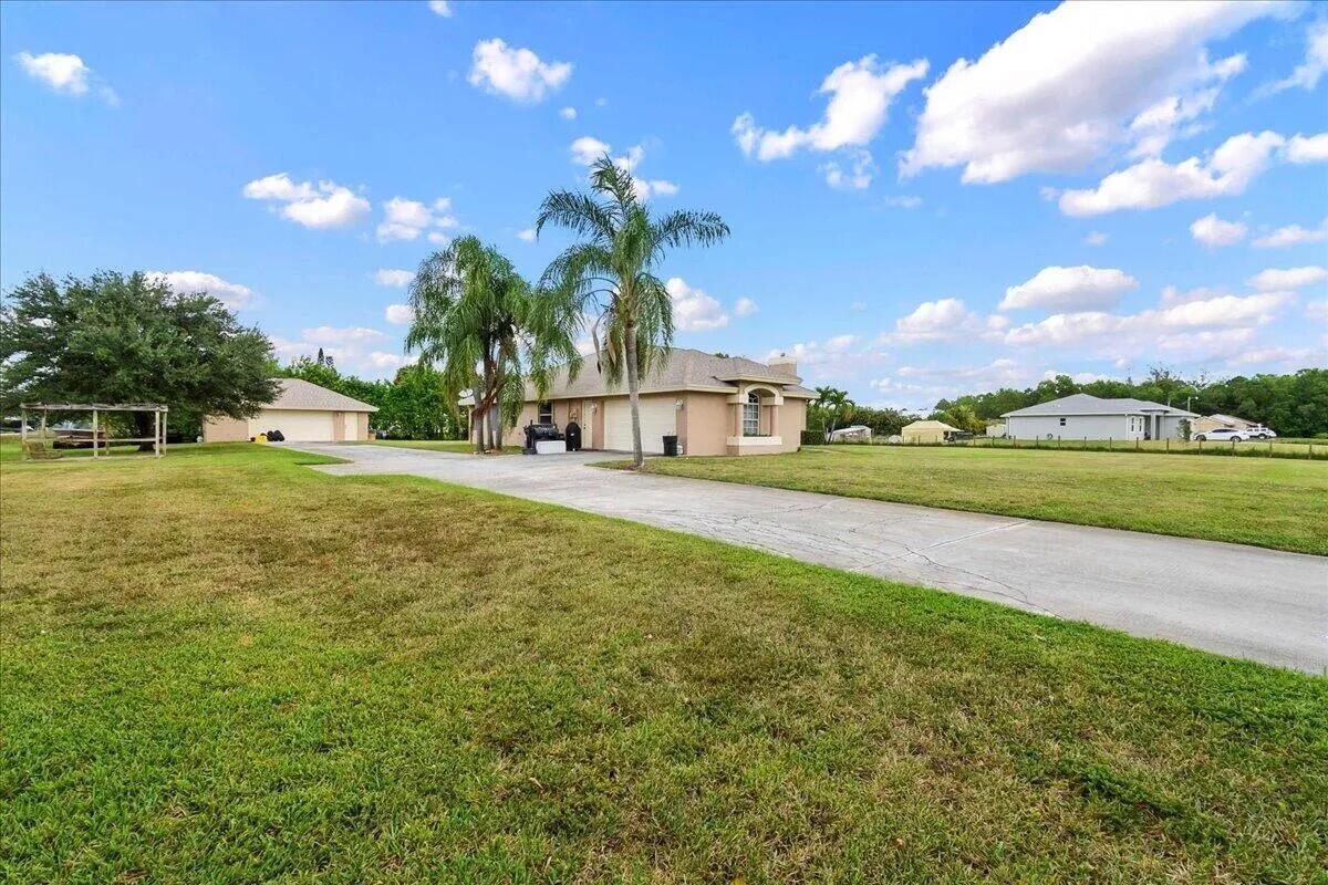 A tan house with a concrete driveway sits on a large, grassy lot under clouds — 13253 N 75th Ln Lane N, FL 33412, FL