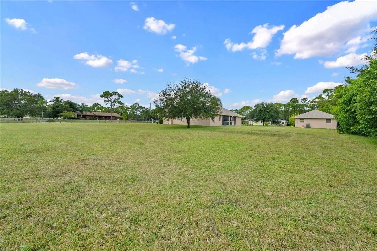 A large, grassy backyard features a single tree and two houses under a blue sky — 13253 N 75th Ln Lane N, FL 33412, FL