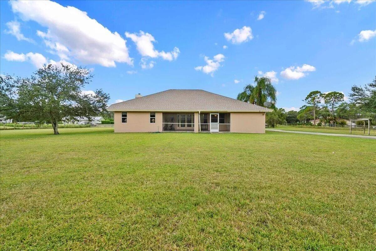 The rear exterior of a single-story beige house features a screened-in patio and large lawn — 13253 N 75th Ln Lane N, FL 33412, FL