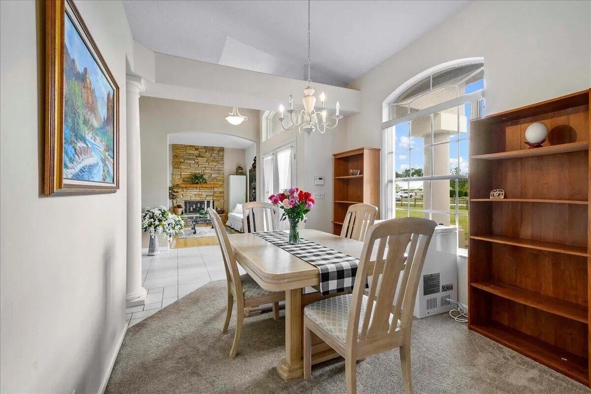 A dining room features a wooden table, chairs, a chandelier, and a stone fireplace beyond — 13253 N 75th Ln Lane N, FL 33412, FL