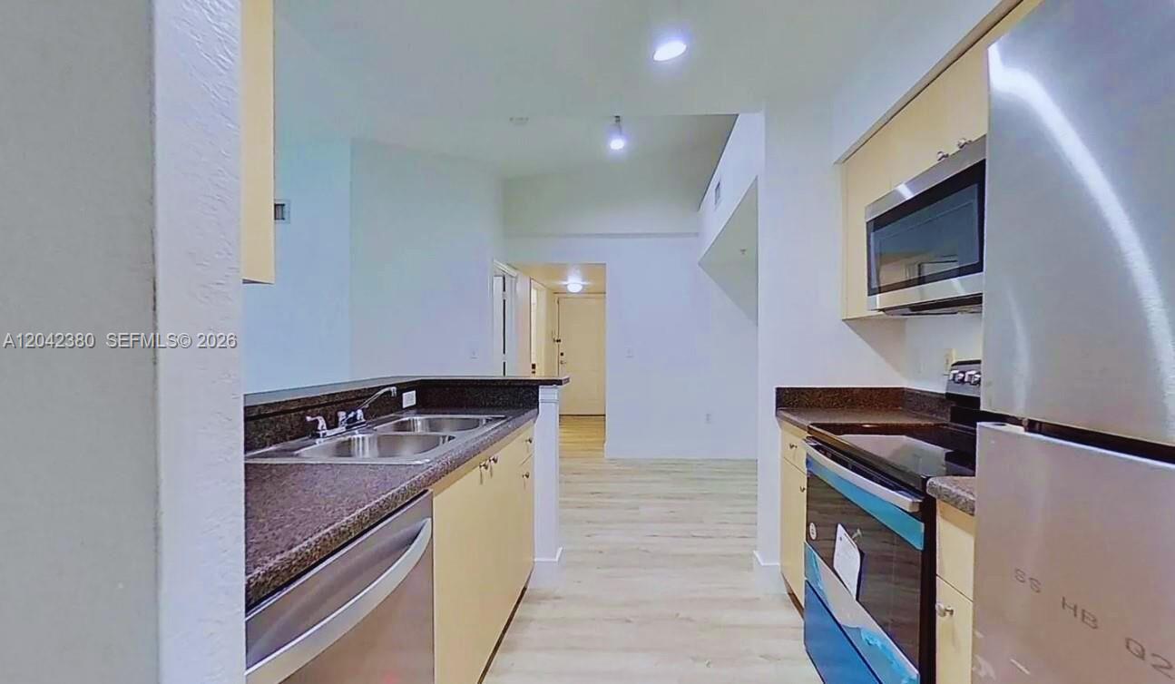 A galley kitchen features light wood cabinets, dark countertops, and stainless steel appliances — 2544 Centergate Dr # 303, Miramar FL 33025, MIRAMAR, FL