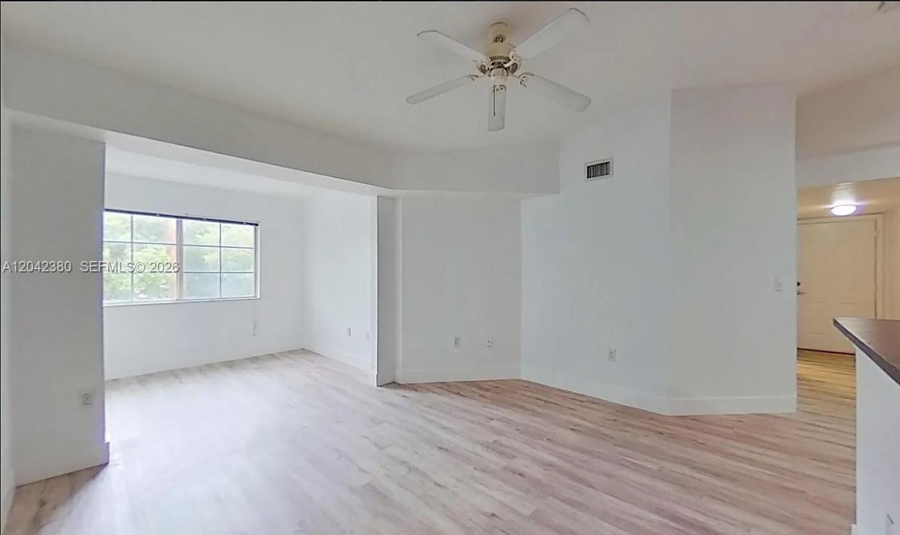 An empty living area features white walls, light wood-look flooring, and a ceiling fan — 2544 Centergate Dr # 303, Miramar FL 33025, MIRAMAR, FL