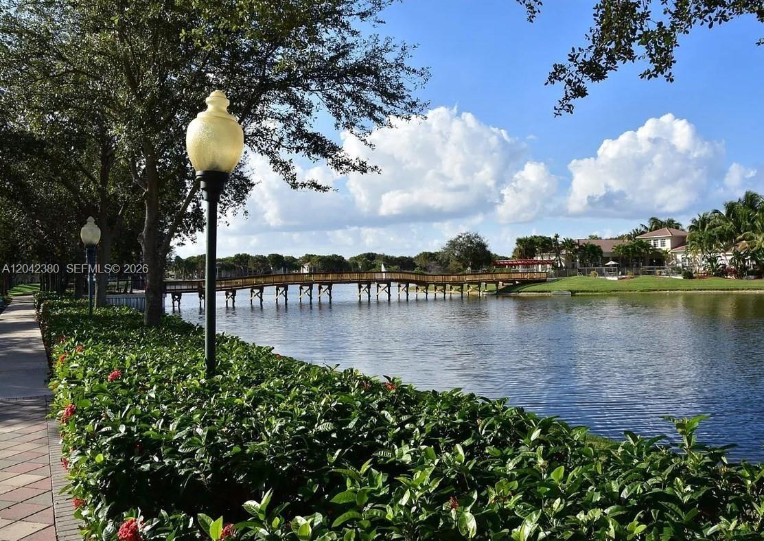 A wooden footbridge spans a lake next to a paved walkway and landscaped bushes — 2544 Centergate Dr # 303, Miramar FL 33025, MIRAMAR, FL