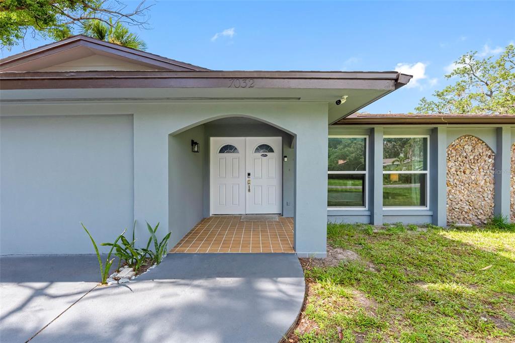 A light gray house exterior features a covered entryway with double doors and stone accents — 7032 MORNINGSTAR LANE, NEW PORT RICHEY, FL