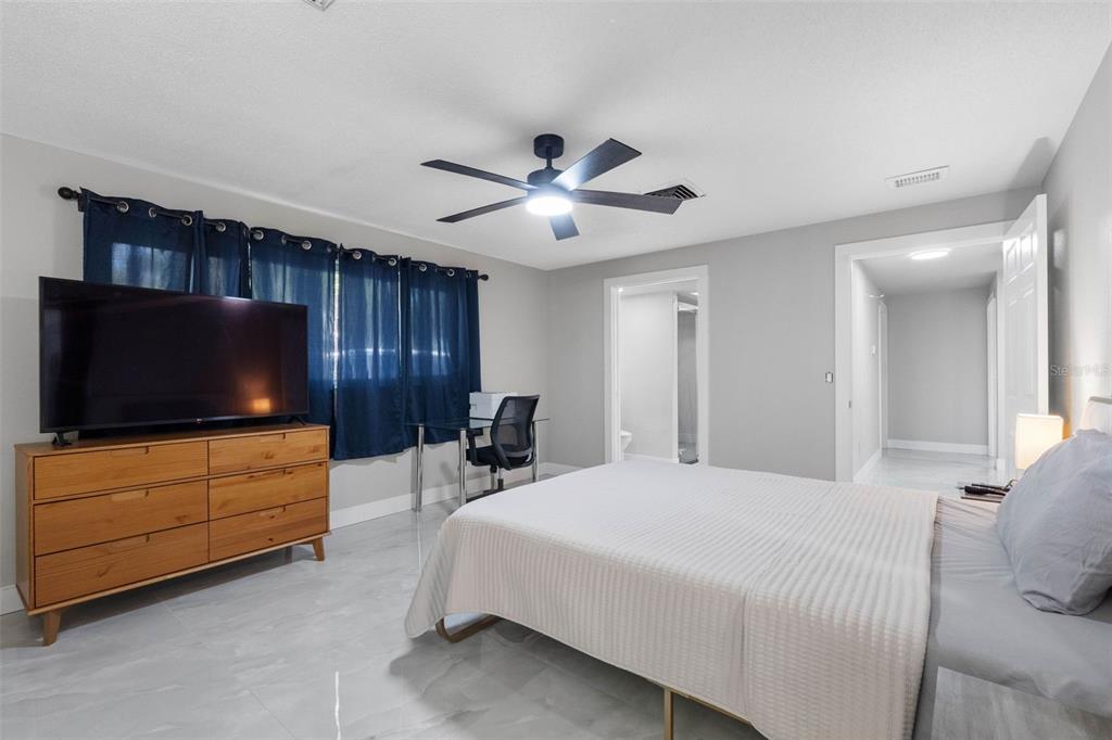 A bedroom features light gray walls, tile flooring, a ceiling fan, and a wooden dresser — 7032 MORNINGSTAR LANE, NEW PORT RICHEY, FL