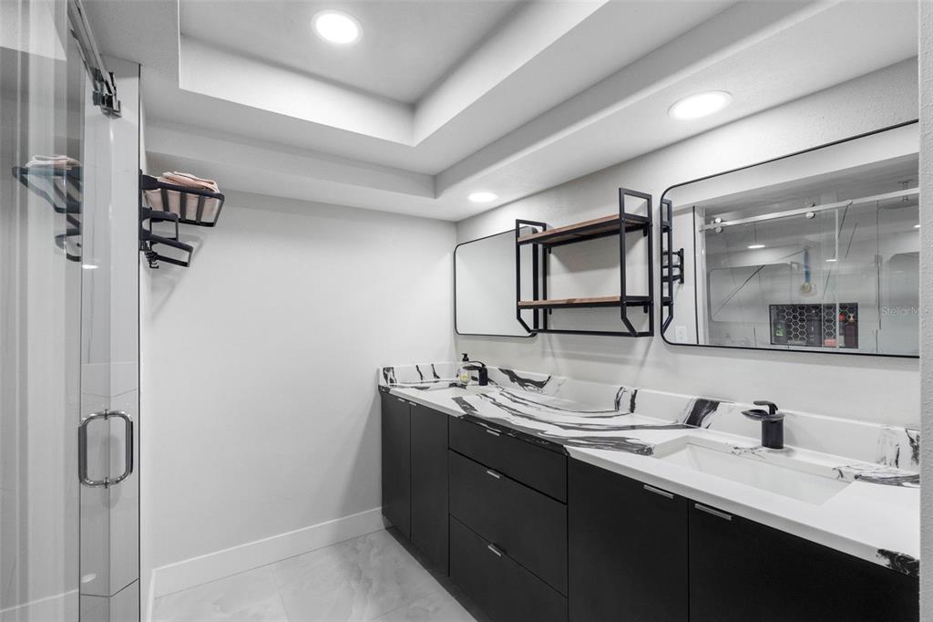 A modern bathroom features a double vanity with black cabinets and a black-and-white marble countertop — 7032 MORNINGSTAR LANE, NEW PORT RICHEY, FL