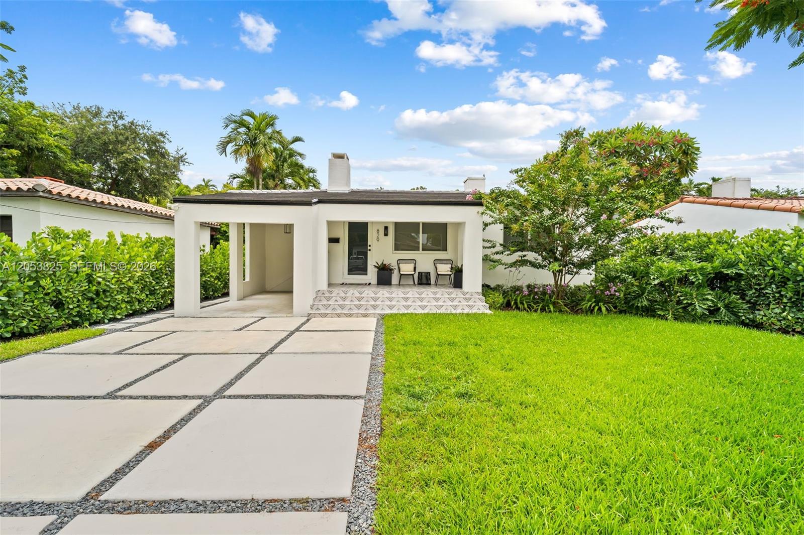 A white single-story house features a covered porch, a paved driveway, and lush landscaping — 829 Granada Groves Ct, Coral Gables FL 33134, CORAL GABLES, FL
