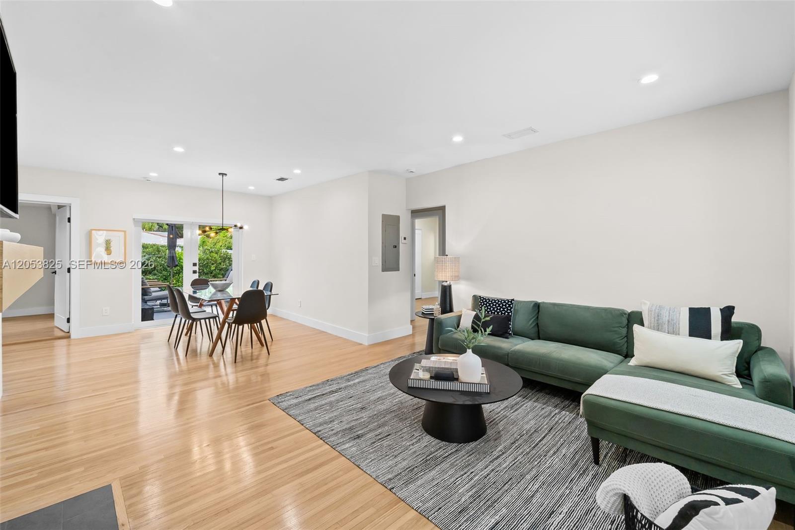 A living and dining area features light wood floors, a green sectional sofa, and glass doors — 829 Granada Groves Ct, Coral Gables FL 33134, CORAL GABLES, FL