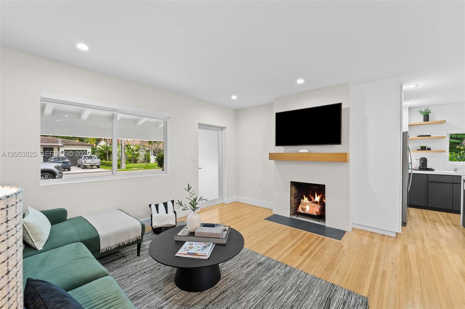 A living room features a fireplace, a wall-mounted television, and a green sectional sofa — 829 Granada Groves Ct, Coral Gables FL 33134, CORAL GABLES, FL