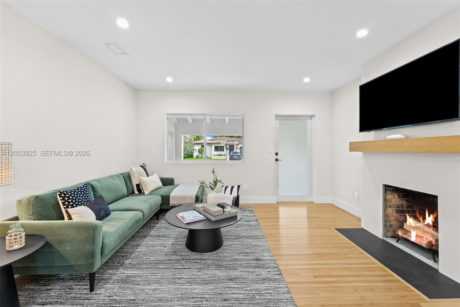 A living room features a green sectional sofa, a fireplace, and light wood flooring — 829 Granada Groves Ct, Coral Gables FL 33134, CORAL GABLES, FL