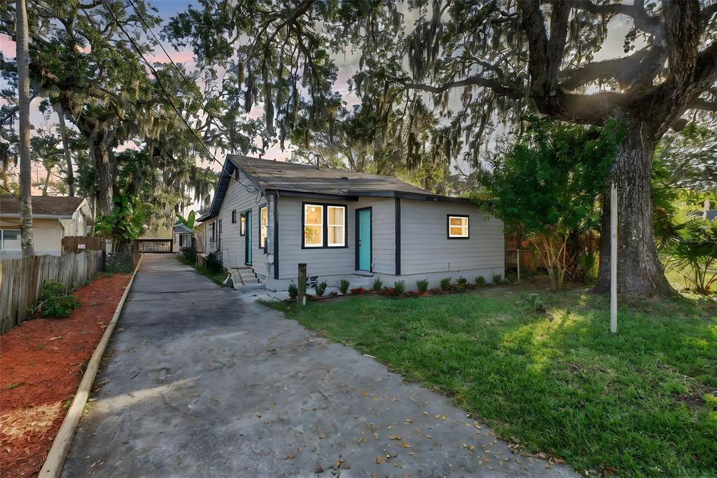 A gray single-story house with a concrete driveway and large oak trees in the yard — 115 PALM PLACE, DAYTONA BEACH, FL