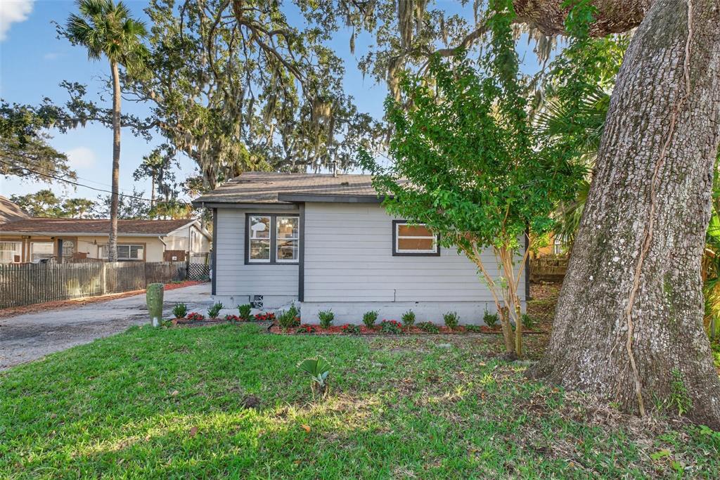 A gray, single-story house with a shingled roof sits behind a lawn and large trees — 115 PALM PLACE, DAYTONA BEACH, FL