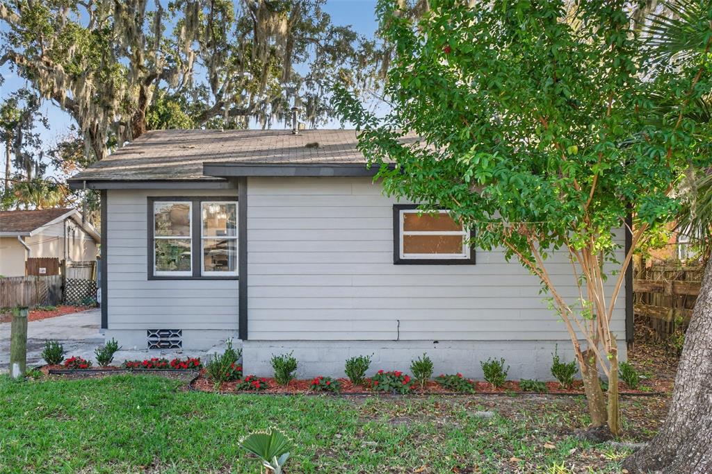 The exterior of a gray, single-story house features a shingled roof and small garden beds — 115 PALM PLACE, DAYTONA BEACH, FL