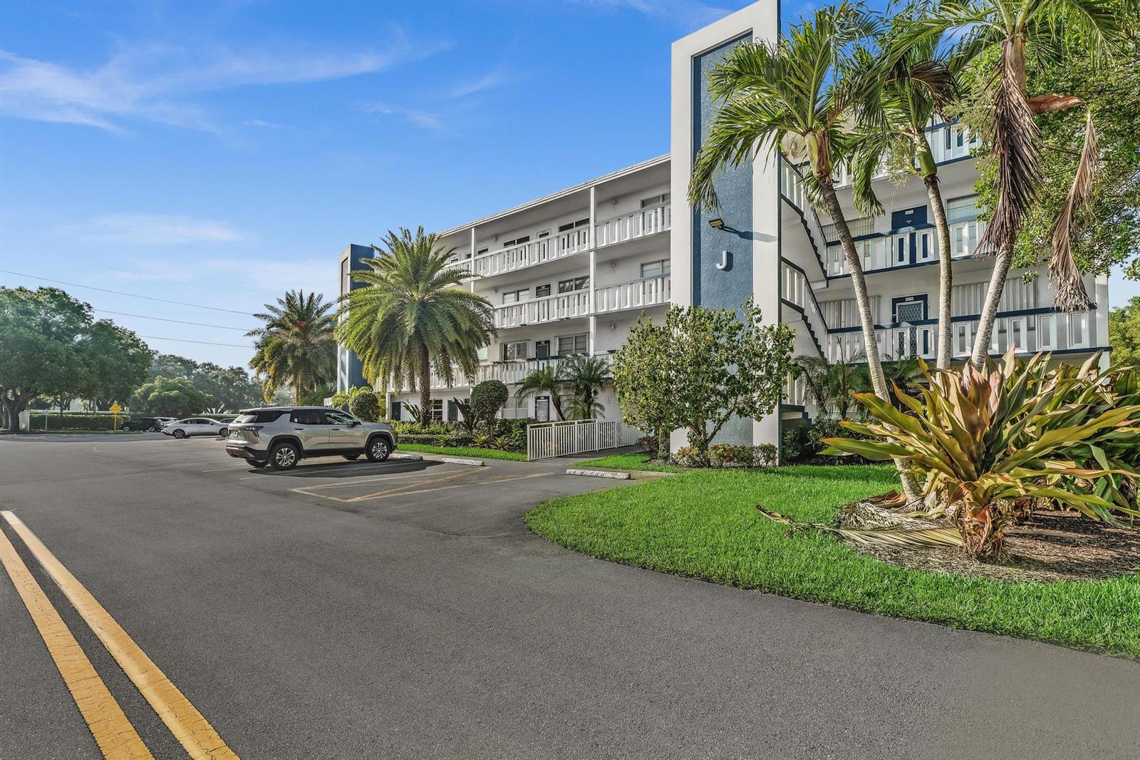 A multi-story apartment building with a parking lot and palm trees under a blue sky — 4001 Upminster J, Deerfield Beach FL 33442, DEERFIELD BEACH, FL