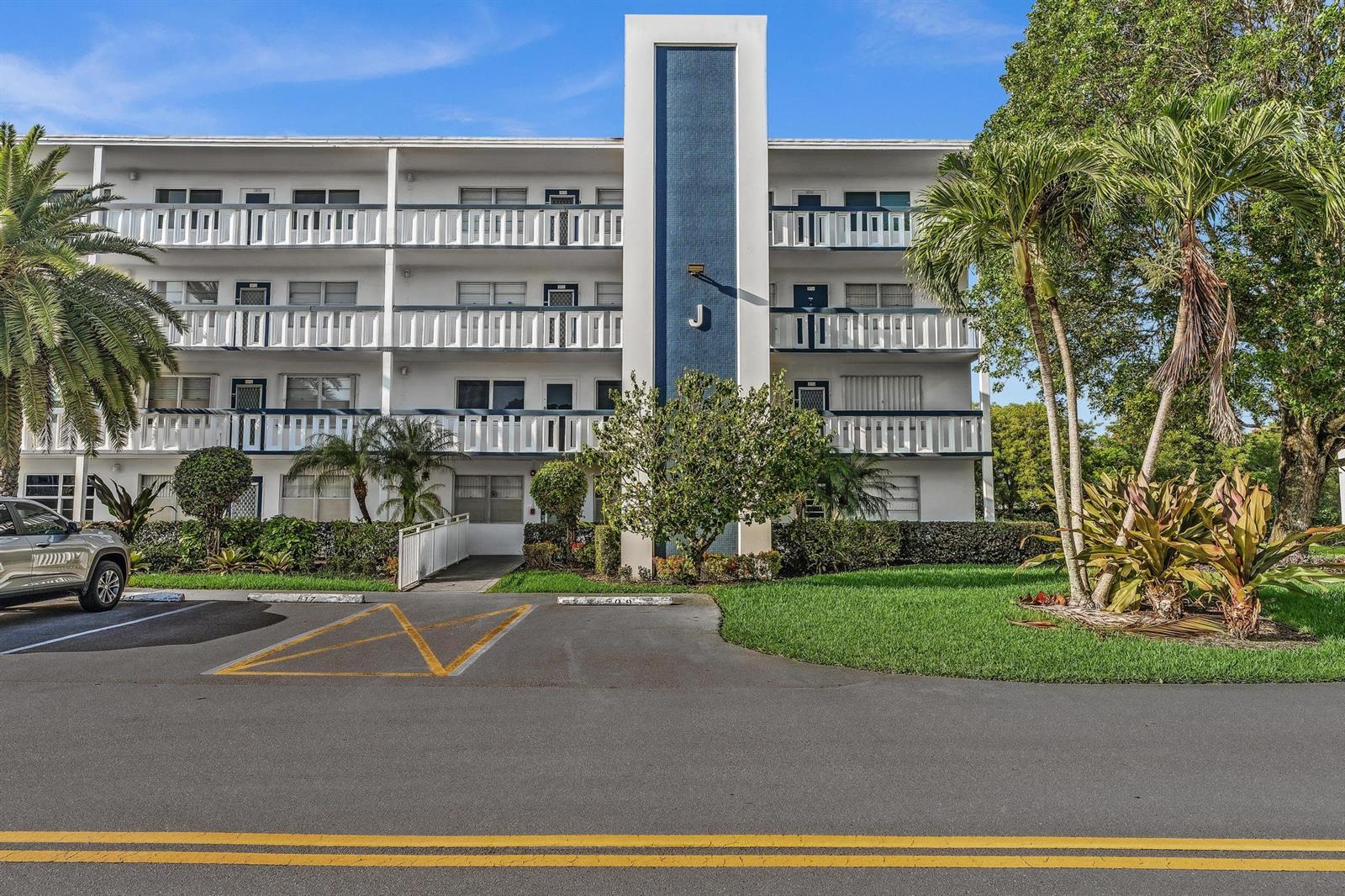 A three-story apartment building with a blue central tower stands behind a parking lot — 4001 Upminster J, Deerfield Beach FL 33442, DEERFIELD BEACH, FL