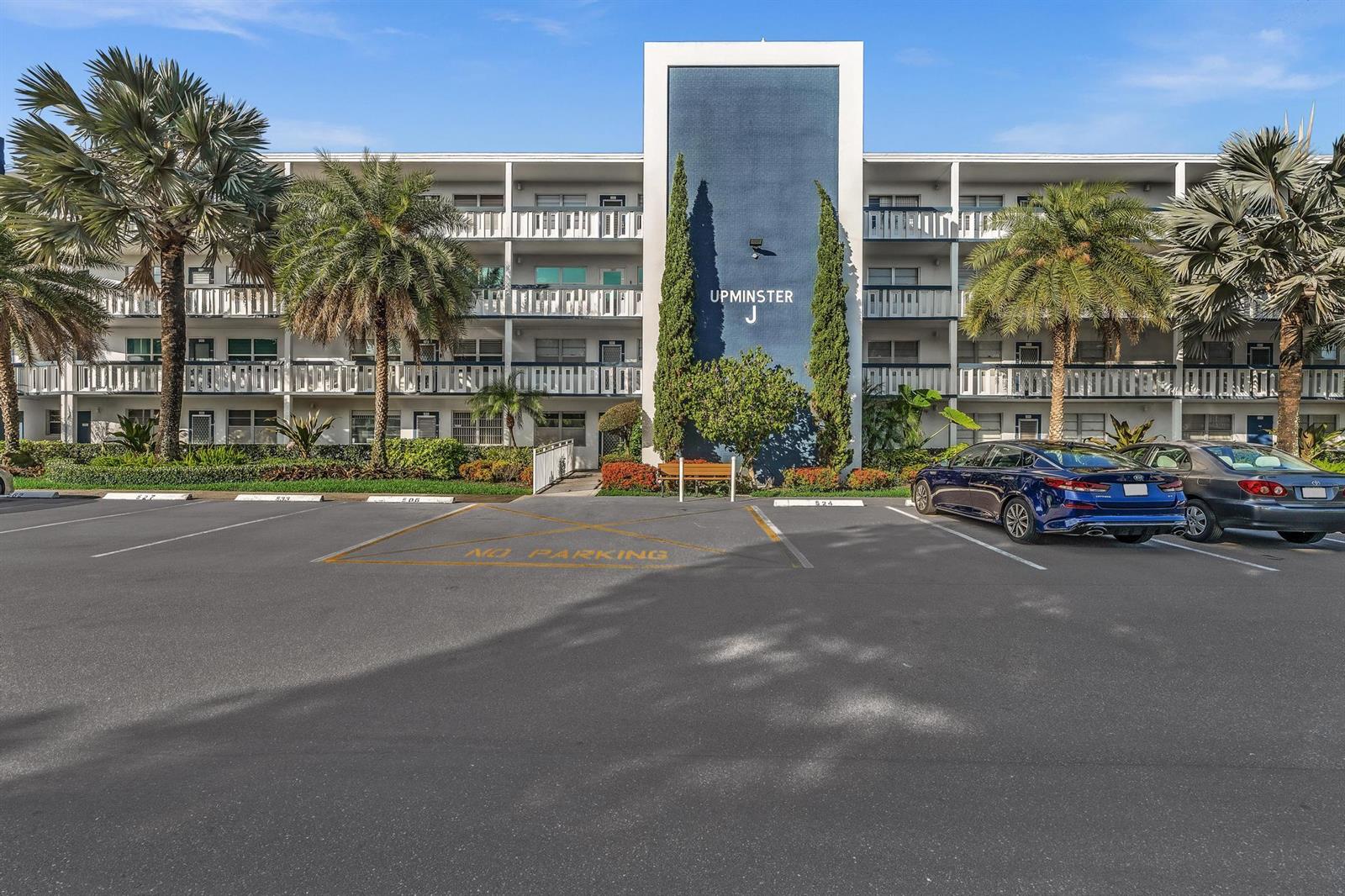 A multi-story apartment building with a blue central facade stands behind a parking lot — 4001 Upminster J, Deerfield Beach FL 33442, DEERFIELD BEACH, FL