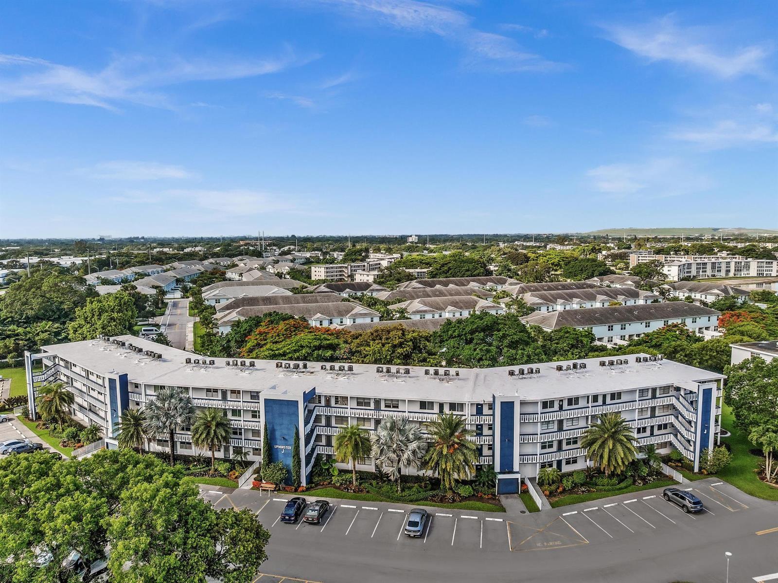 An aerial view of a multi-story apartment building with a parking lot and surrounding greenery — 4001 Upminster J, Deerfield Beach FL 33442, DEERFIELD BEACH, FL
