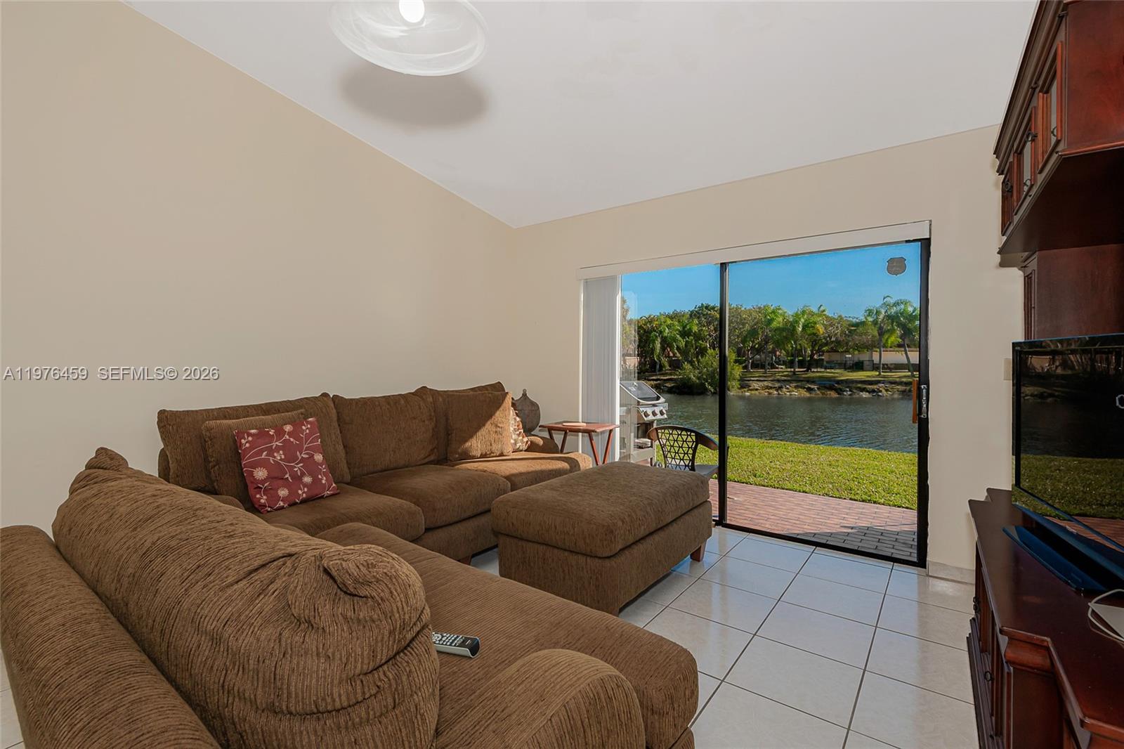 A living room with brown sofas, tile flooring, and a sliding door overlooking a lake — 840 SW 120th Way, Davie FL 33325, DAVIE, FL