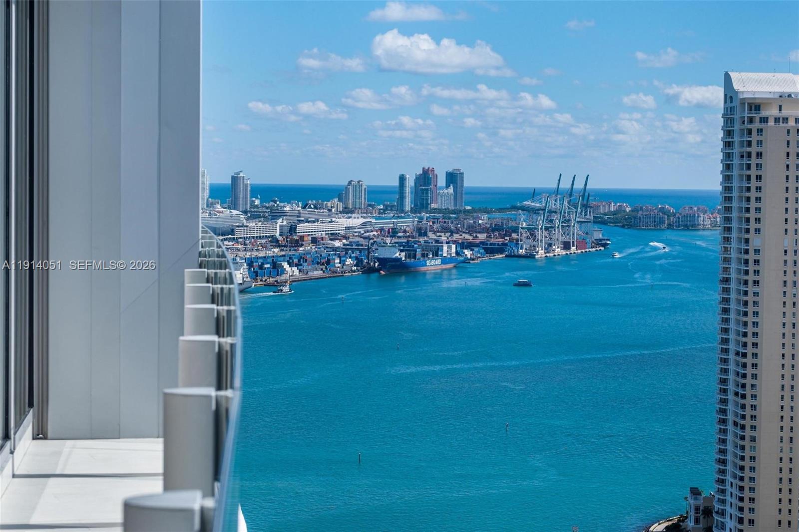 A high-rise balcony overlooks a busy shipping port, a bay, and a distant city skyline — 300 Biscayne Boulevard Way # 3506W, Miami FL 33131, MIAMI, FL
