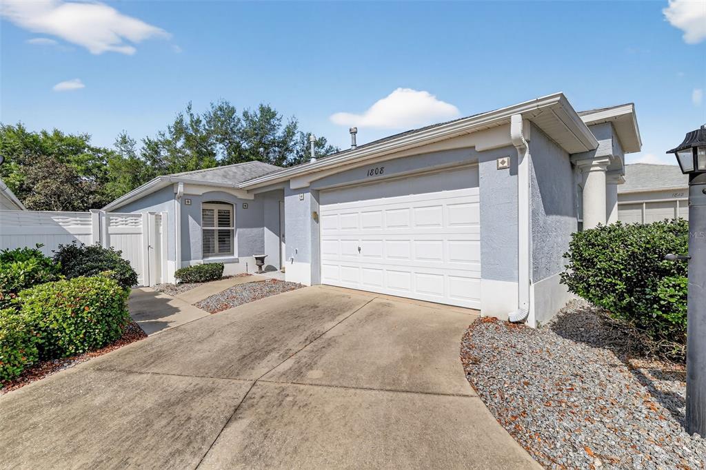 A single-story house with a white garage door, light blue stucco exterior, and concrete driveway — 1808 PEACHTREE AVENUE, THE VILLAGES, FL