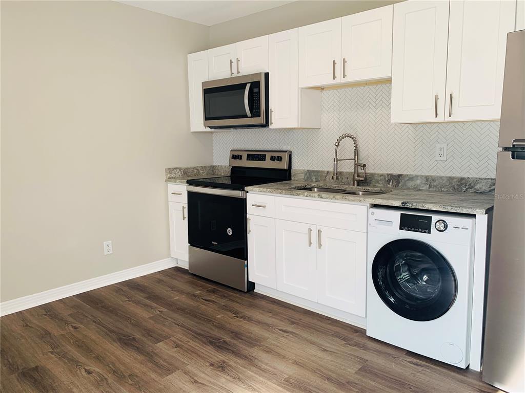 A kitchen features white cabinets, stainless steel appliances, a herringbone backsplash, and a built-in washer — 3805 W LEONA STREET UNIT 2, TAMPA, FL