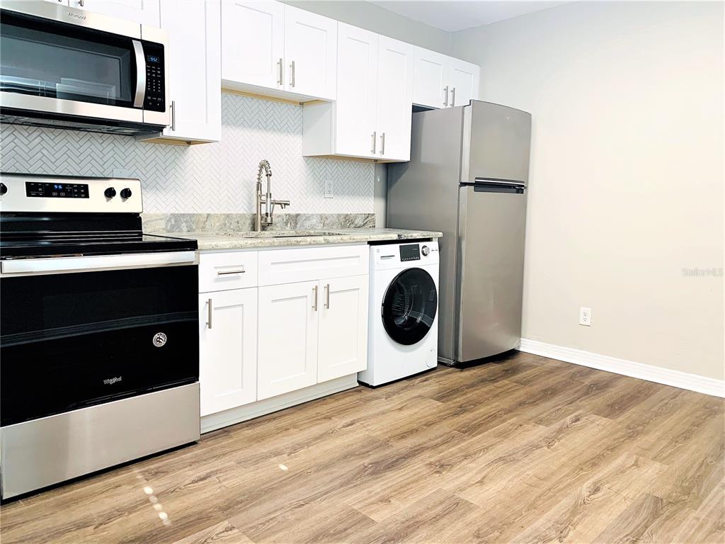A kitchen features white cabinets, stainless steel appliances, a herringbone backsplash, and a built-in washer — 3805 W LEONA STREET UNIT 2, TAMPA, FL