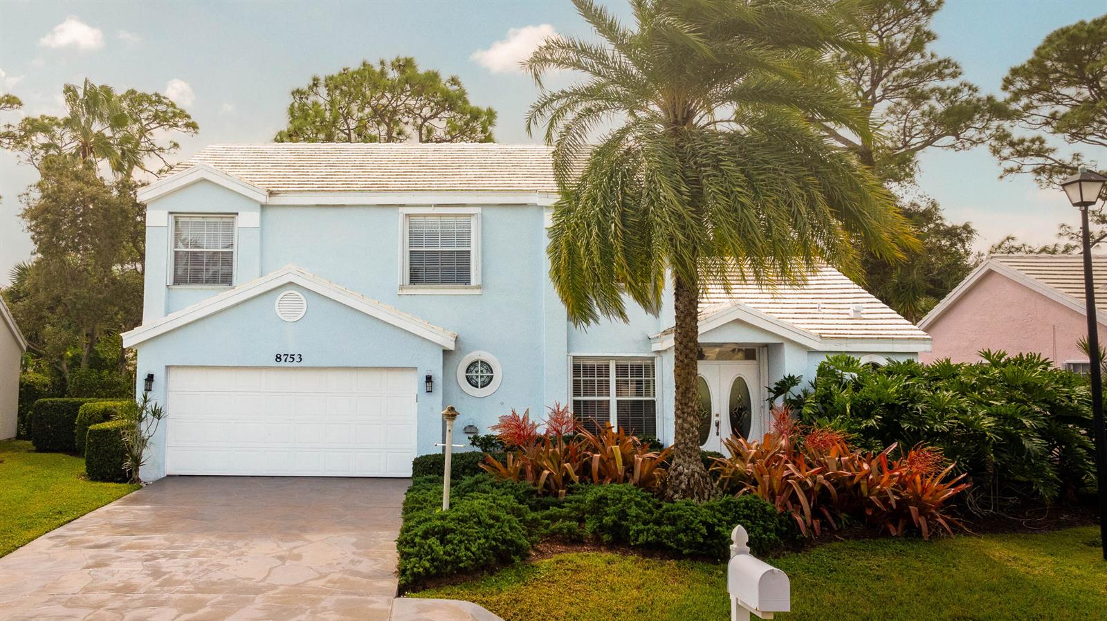 A two-story light blue house with a white garage, palm tree, and landscaped front yard — 8753 SE Riverfront Terrace, Jupiter FL 33469, JUPITER, FL