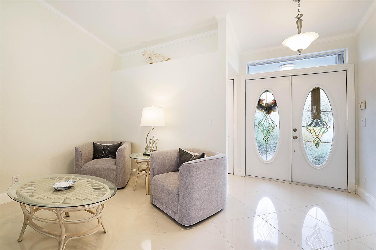 A bright entryway features a seating area with two gray armchairs, glass tables, and tiled floors — 8753 SE Riverfront Terrace, Jupiter FL 33469, JUPITER, FL
