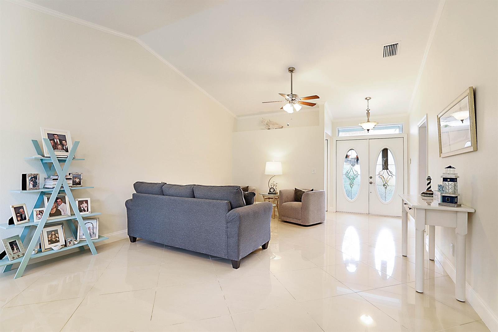 A bright living room features a grey sofa, a light blue display shelf, and tile flooring — 8753 SE Riverfront Terrace, Jupiter FL 33469, JUPITER, FL