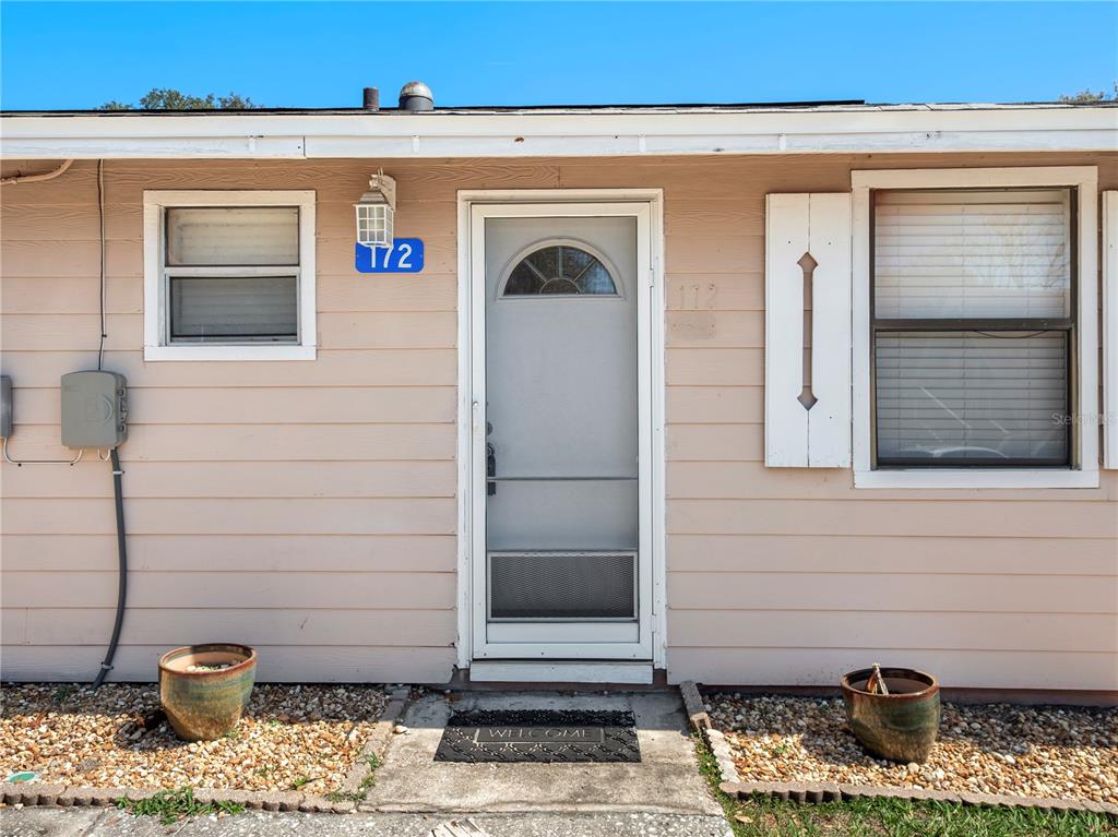 The exterior of a single-story home features light-colored siding, a front door, and two windows — 10301 S U S HIGHWAY 27 UNIT 172, CLERMONT, FL