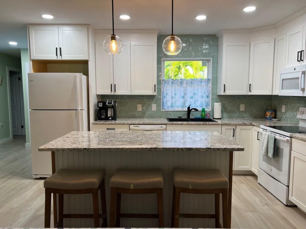 A kitchen with white cabinets, granite countertops, a central island, and a light green backsplash — 311 66TH STREET, BRADENTON BEACH, FL