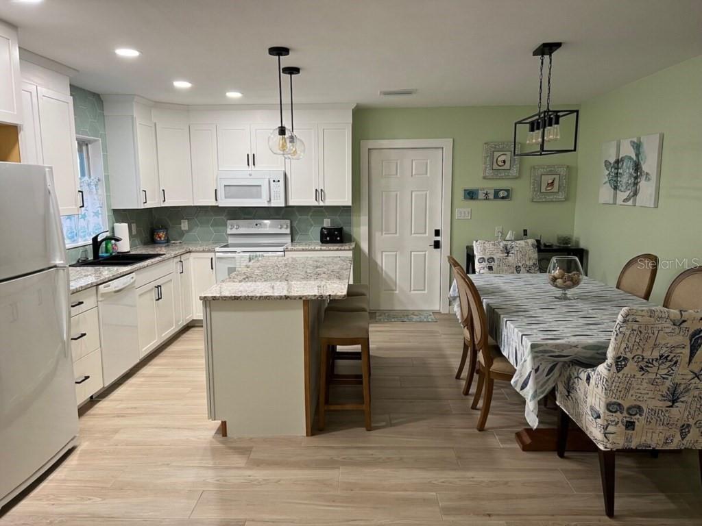 A kitchen with white cabinets, granite countertops, and an island next to a dining area — 311 66TH STREET, BRADENTON BEACH, FL
