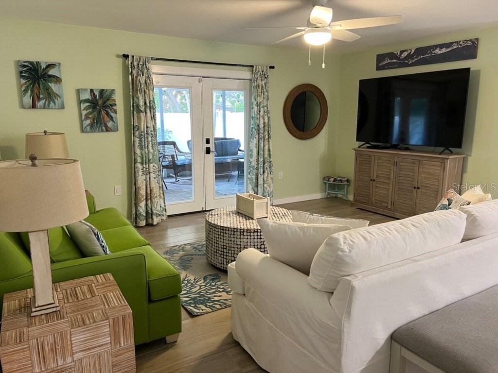 A living room features a green sofa, white sectional, television, and glass doors to a patio — 311 66TH STREET, BRADENTON BEACH, FL
