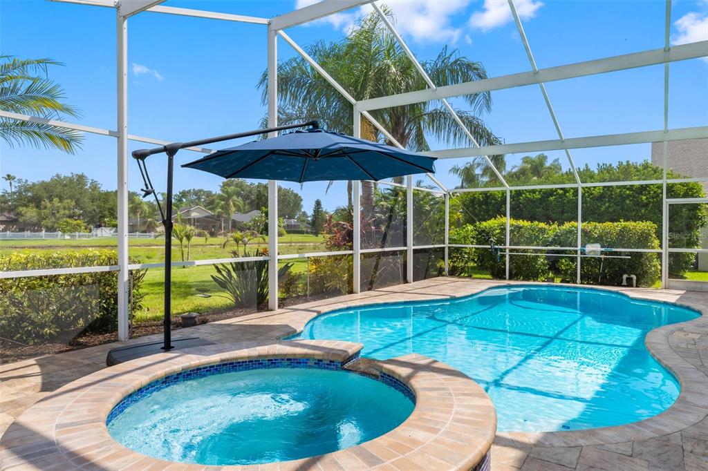 A screened-in pool and spa area with a blue cantilever umbrella on a paved patio — 9104 CYPRESS KEEP LANE, ODESSA, FL