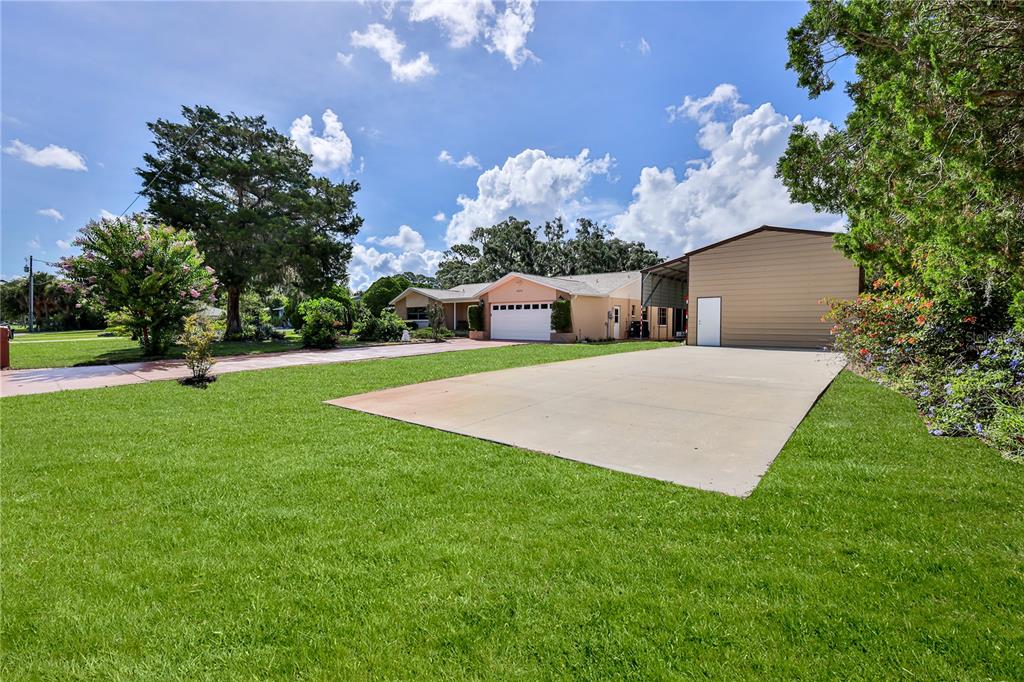 A single-story house with a garage and a large concrete driveway sits on a lawn — 8270 SYCAMORE DRIVE, NEW PORT RICHEY, FL