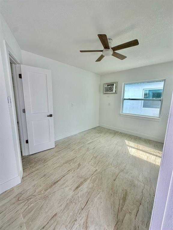An empty bedroom features white walls, a ceiling fan, a window unit, and tiled flooring — 150 147TH AVENUE E, MADEIRA BEACH, FL
