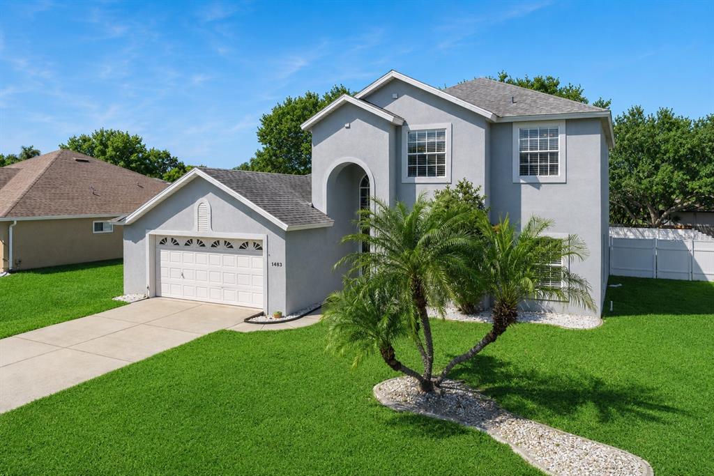 A two-story gray house with a garage, palm tree, and green lawn under a blue sky — 1483 SURREY PARK DRIVE, PORT ORANGE, FL