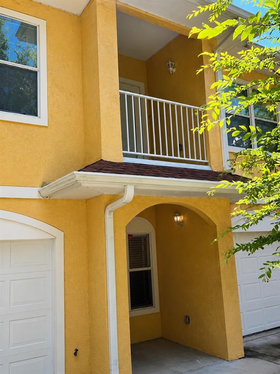 A yellow two-story building exterior features a white balcony, a covered entryway, and garage doors — 518 NW 39 ROAD, GAINESVILLE, FL