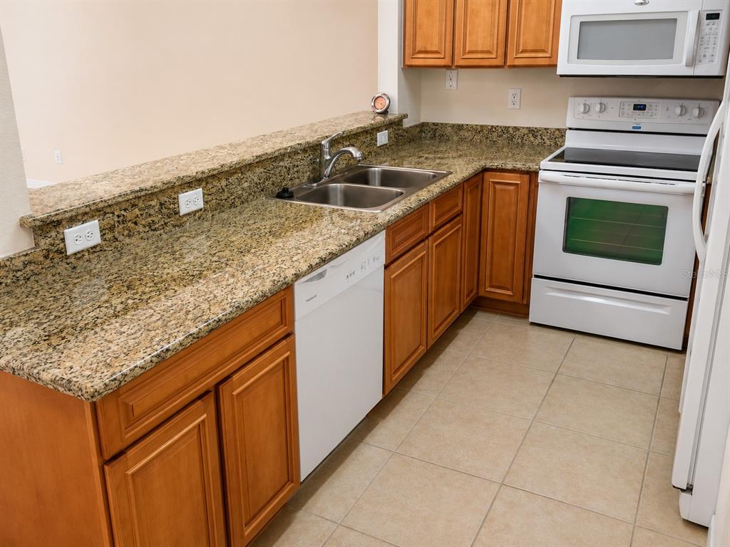 A kitchen features wood cabinets, granite countertops, tile flooring, and white appliances — 518 NW 39 ROAD, GAINESVILLE, FL