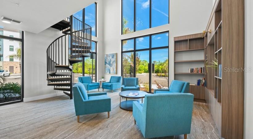 A modern lounge features a spiral staircase, floor-to-ceiling windows, and several blue armchairs — 8925 77TH TERRACE E UNIT B3-S, LAKEWOOD RANCH, FL