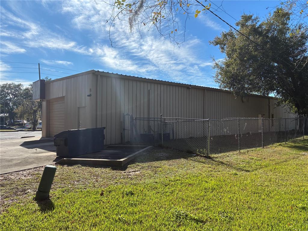 A tan metal industrial building features a roll-up door, a dumpster, and a chain-link fence — 5745 PERSHING AVENUE, ORLANDO, FL