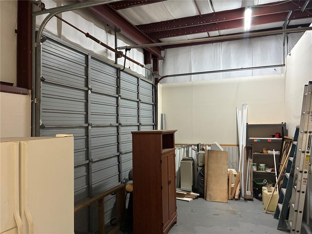 A storage room features a large metal roll-up door, exposed steel beams, and various items — 5745 PERSHING AVENUE, ORLANDO, FL