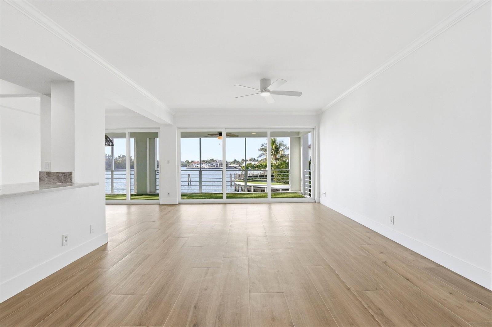 An empty living room with light wood flooring, white walls, and sliding doors overlooking water — 850 NE Spanish River Boulevard # 0240, Boca Raton FL 33431, BOCA RATON, FL