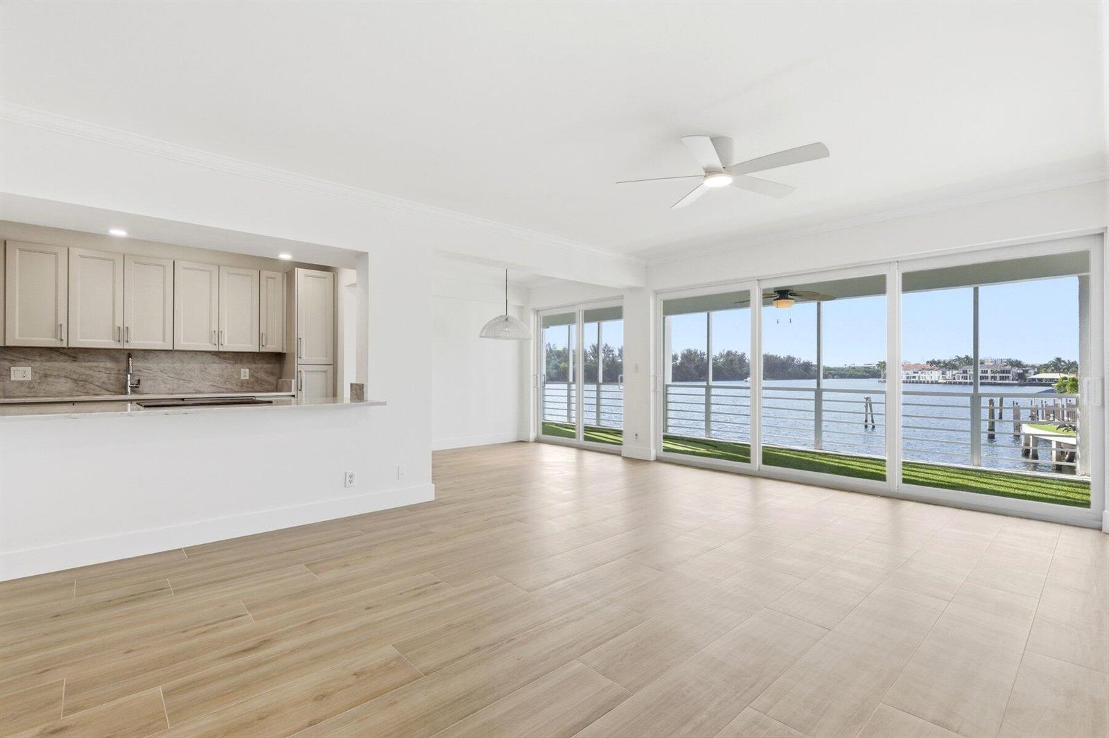 A bright living area with light wood-look tile floors, a kitchen pass-through, and waterfront views — 850 NE Spanish River Boulevard # 0240, Boca Raton FL 33431, BOCA RATON, FL