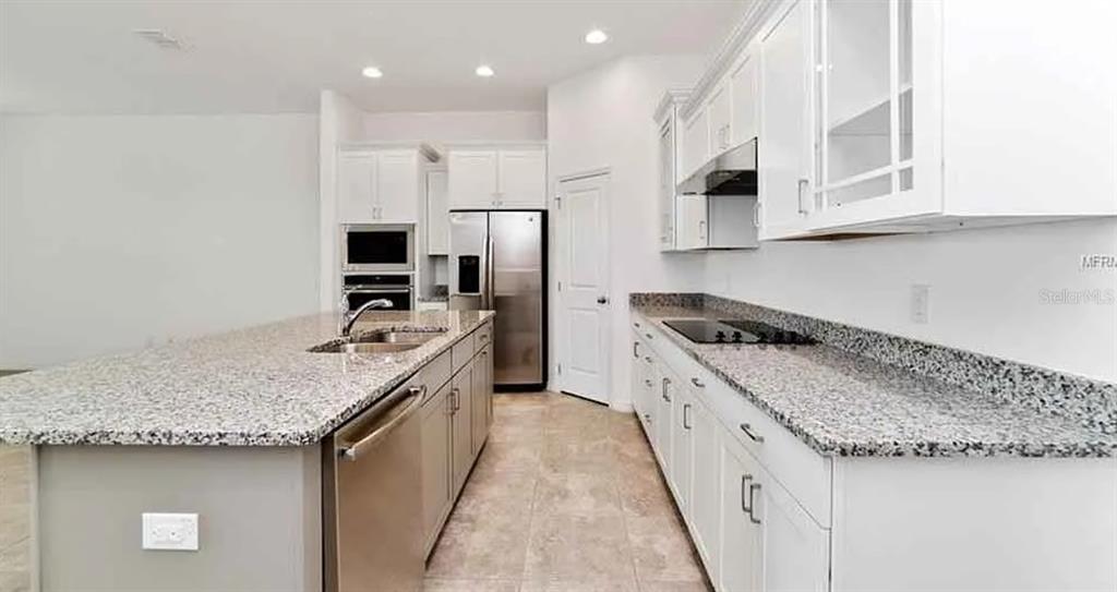 A kitchen features white cabinets, granite countertops, a center island, and stainless steel appliances — 5305 JUBILOSO DRIVE, ST CLOUD, FL