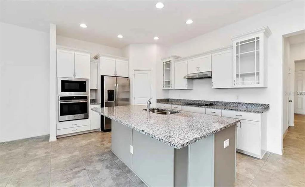 A kitchen with white cabinets, granite countertops, a central island, and stainless steel appliances — 5305 JUBILOSO DRIVE, ST CLOUD, FL