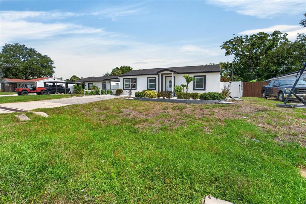 A single-story white house with a dark roof sits behind a large, grassy front yard — 4711 W LAWN AVENUE, TAMPA, FL