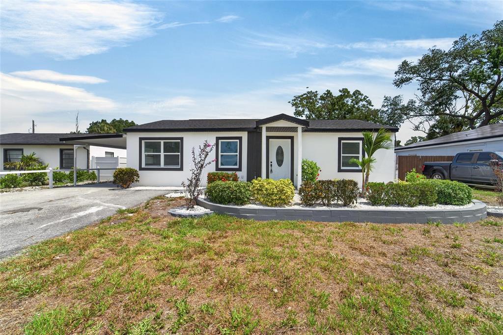 A single-story house with a white exterior, dark roof, and a curved front garden bed — 4711 W LAWN AVENUE, TAMPA, FL