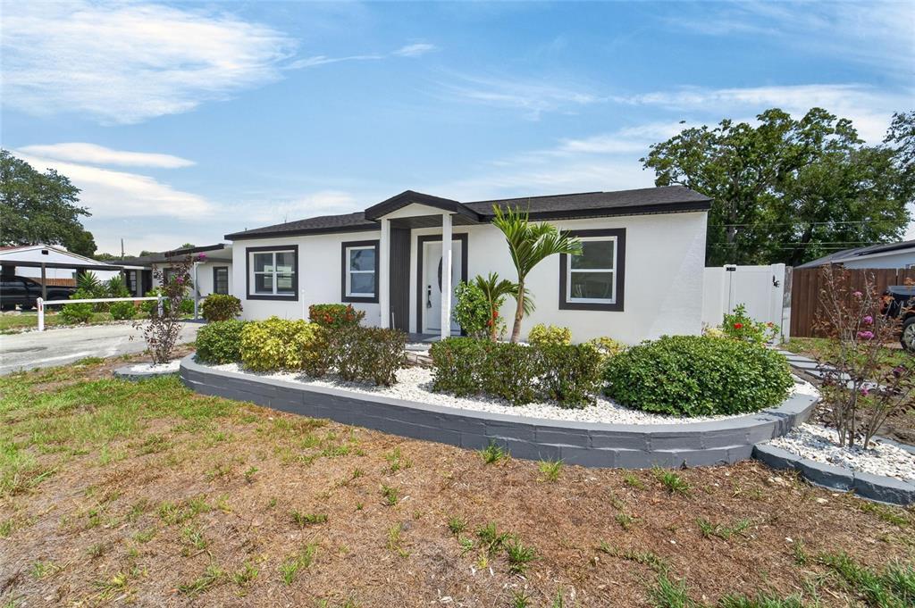 A white single-story house with a dark roof and a gray stone retaining wall — 4711 W LAWN AVENUE, TAMPA, FL